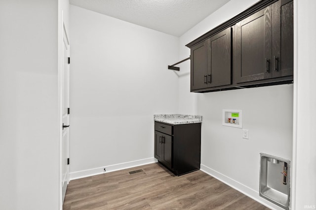 laundry room featuring light wood-type flooring, cabinets, a textured ceiling, and washer hookup