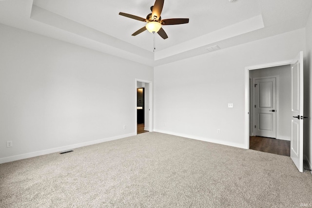 carpeted spare room with ceiling fan and a raised ceiling