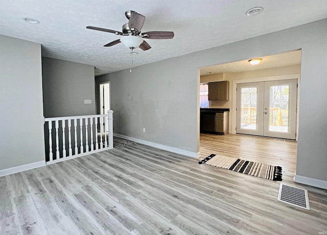 empty room with light wood-type flooring, a textured ceiling, ceiling fan, and french doors