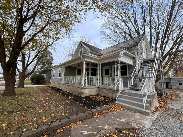 view of front of property featuring stairs, covered porch, and roof with shingles