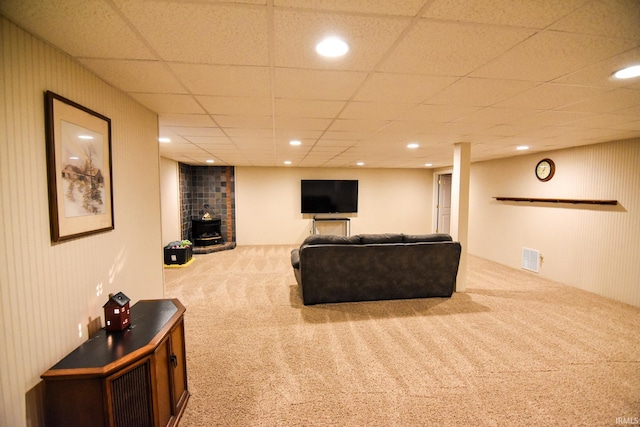 living room with a wood stove, a paneled ceiling, and light carpet