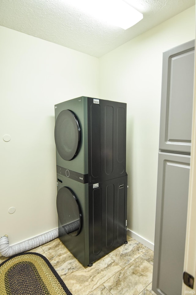 clothes washing area featuring cabinets, stacked washer and dryer, and a textured ceiling