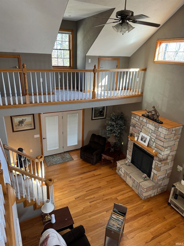 living room with a stone fireplace, high vaulted ceiling, ceiling fan, and light hardwood / wood-style flooring