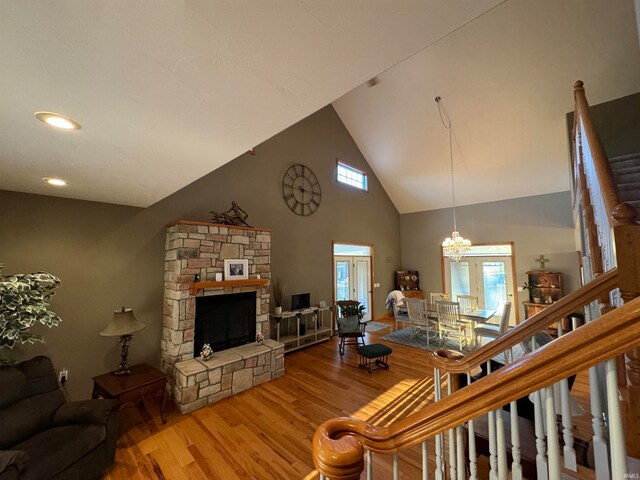 living room with hardwood / wood-style floors, a stone fireplace, high vaulted ceiling, and a notable chandelier