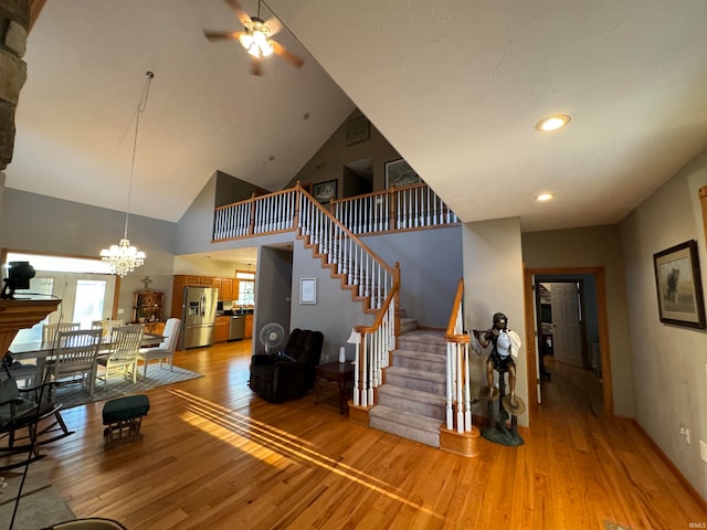 stairs with hardwood / wood-style floors, ceiling fan with notable chandelier, and high vaulted ceiling