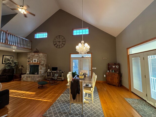 dining space with light hardwood / wood-style floors, a stone fireplace, ceiling fan with notable chandelier, and high vaulted ceiling