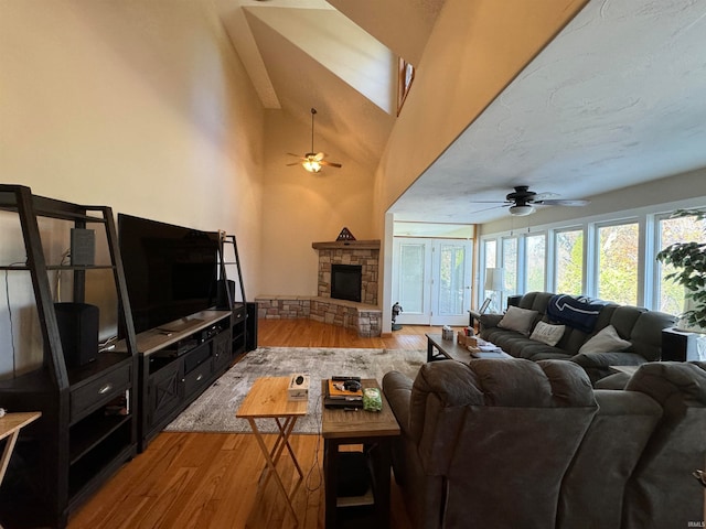 living room featuring ceiling fan, light hardwood / wood-style floors, a stone fireplace, and high vaulted ceiling