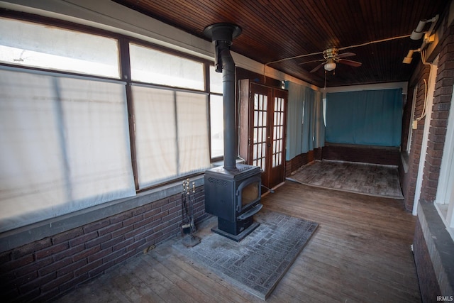 unfurnished sunroom featuring a wood stove, ceiling fan, and wooden ceiling