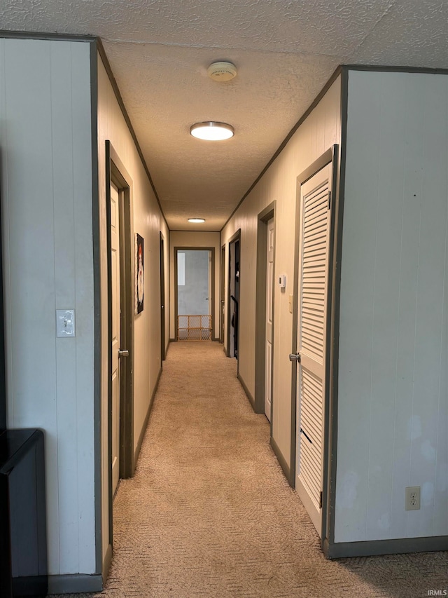 hallway featuring wood walls, light colored carpet, and a textured ceiling