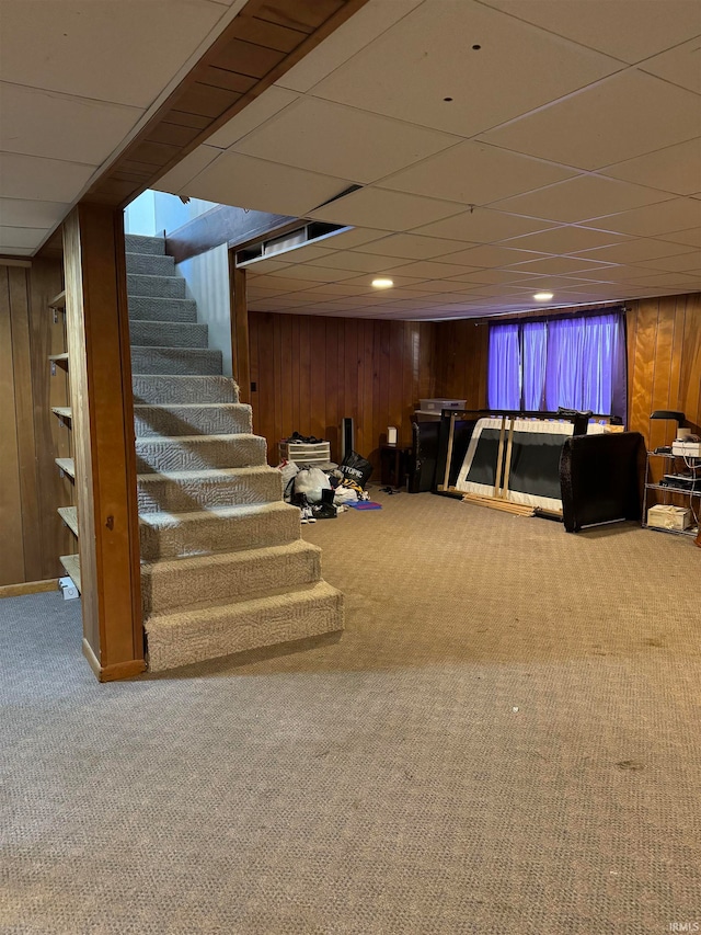 basement with carpet floors, a drop ceiling, and wooden walls