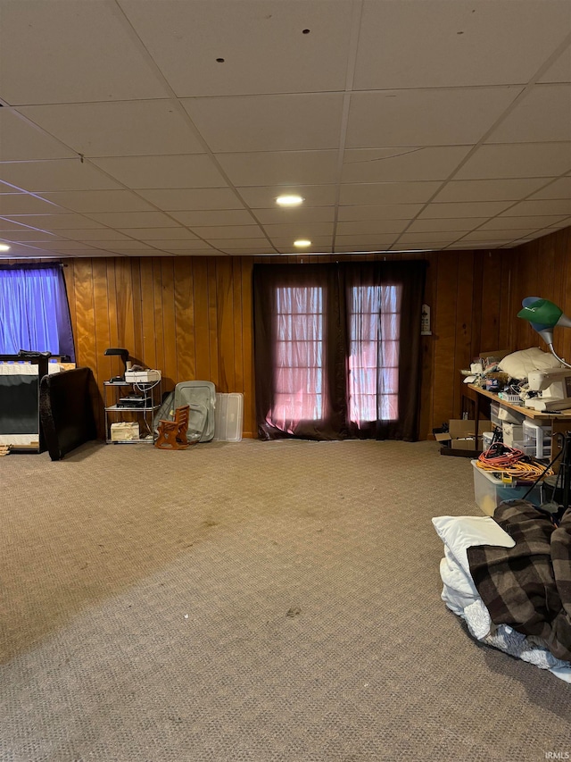 sitting room with carpet, a drop ceiling, and wood walls