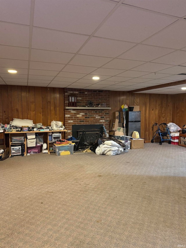 basement with carpet, a drop ceiling, wood walls, a fireplace, and stainless steel refrigerator