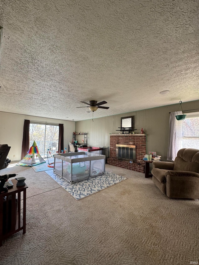 living room with carpet flooring, ceiling fan, a fireplace, and a textured ceiling