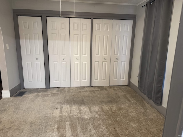 unfurnished bedroom featuring multiple closets, carpet, and ornamental molding