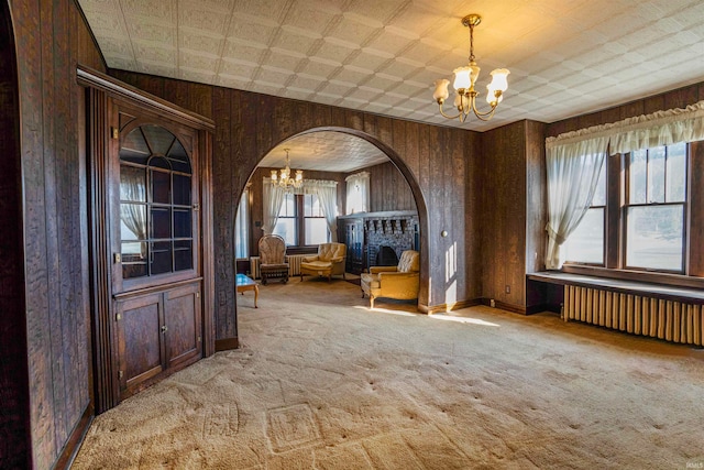 unfurnished dining area featuring radiator, wooden walls, light carpet, and an inviting chandelier