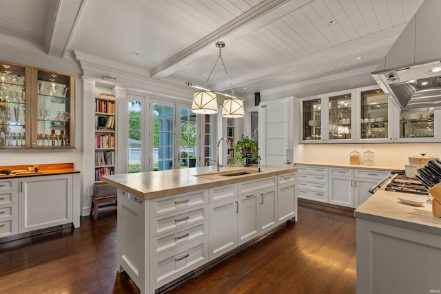 kitchen featuring dark wood-type flooring, an island with sink, beam ceiling, white cabinetry, and decorative light fixtures