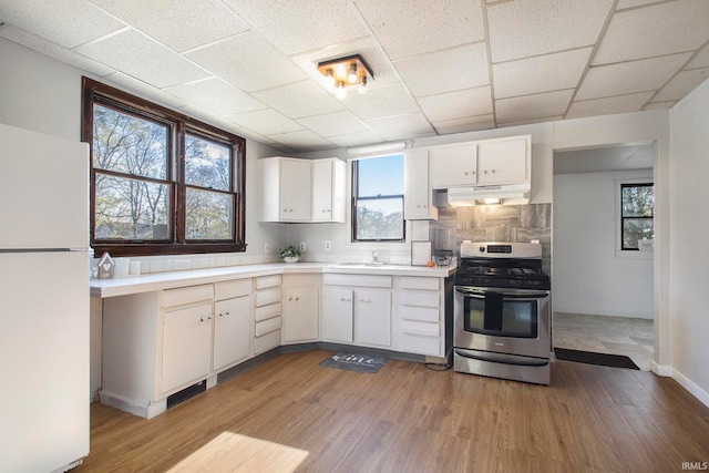 kitchen with white cabinets, light hardwood / wood-style flooring, stainless steel range, tasteful backsplash, and white fridge