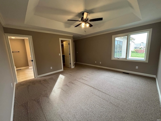 unfurnished bedroom with light carpet, ceiling fan, crown molding, a raised ceiling, and a walk in closet