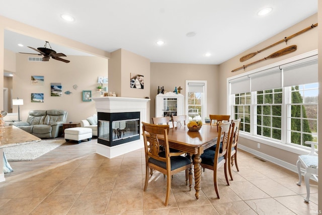 dining room with a multi sided fireplace, ceiling fan, and light wood-type flooring