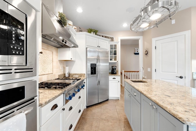 kitchen featuring light stone countertops, white cabinetry, sink, stainless steel appliances, and wall chimney range hood