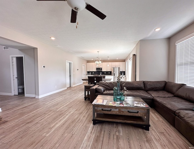 living room with light hardwood / wood-style floors, ceiling fan with notable chandelier, and a textured ceiling