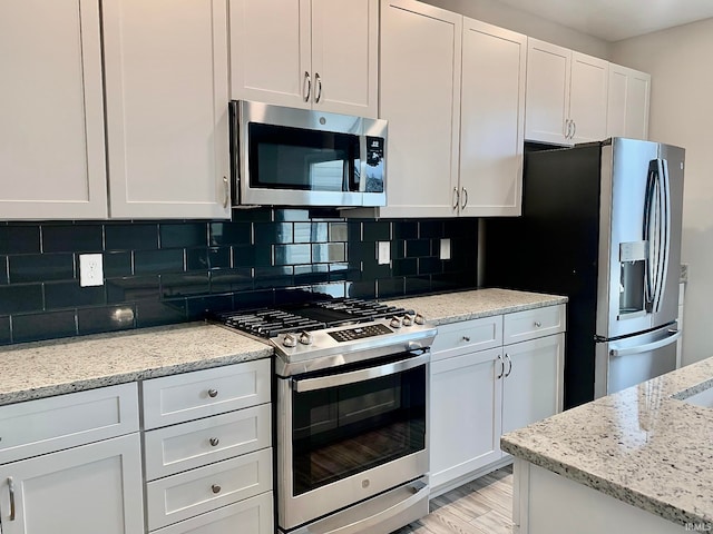 kitchen featuring white cabinetry, appliances with stainless steel finishes, light hardwood / wood-style floors, and light stone counters