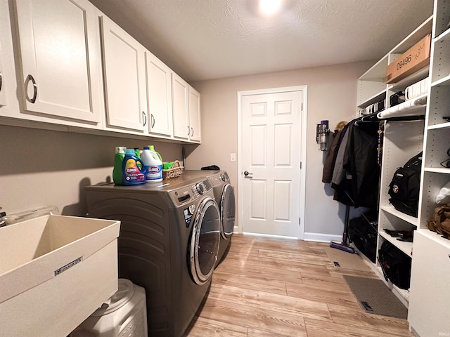 laundry area featuring light hardwood / wood-style floors, cabinets, a textured ceiling, sink, and washer and clothes dryer