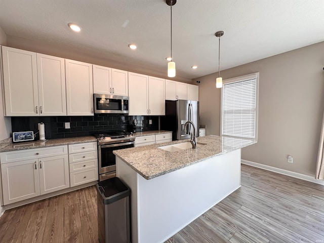 kitchen featuring light hardwood / wood-style floors, stainless steel appliances, white cabinets, sink, and decorative light fixtures