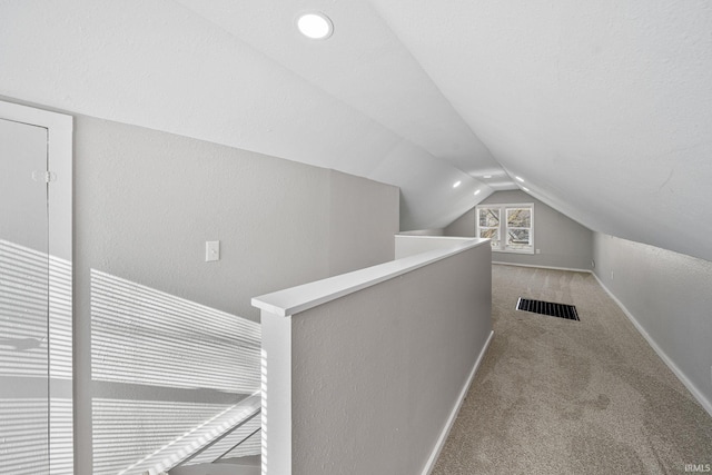 corridor with vaulted ceiling, light colored carpet, and a textured ceiling