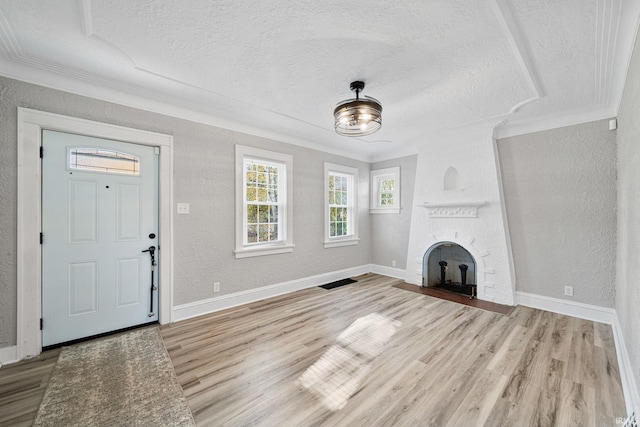 unfurnished living room featuring a fireplace, a textured ceiling, light hardwood / wood-style flooring, and ornamental molding