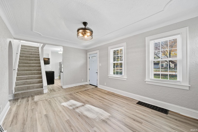 foyer entrance featuring light hardwood / wood-style floors, a textured ceiling, and crown molding