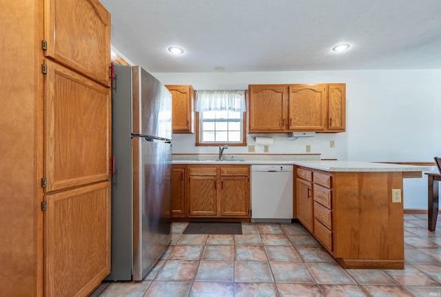 kitchen with dishwasher, kitchen peninsula, sink, light tile patterned floors, and stainless steel refrigerator