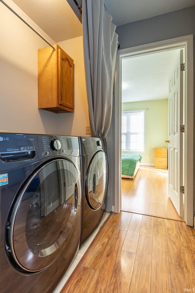 clothes washing area featuring cabinets, light hardwood / wood-style floors, and washer and clothes dryer