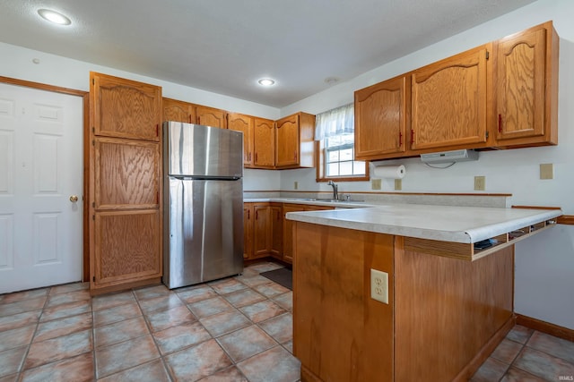 kitchen featuring kitchen peninsula, sink, stainless steel refrigerator, and light tile patterned floors