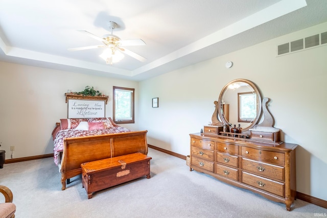 bedroom with light colored carpet, ceiling fan, and a raised ceiling