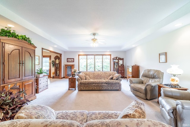 living room featuring ceiling fan, light colored carpet, and a raised ceiling