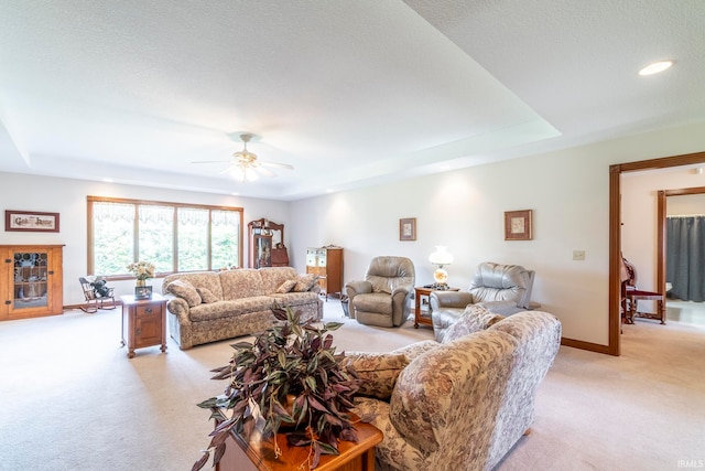 living room with a tray ceiling, a textured ceiling, light carpet, and ceiling fan