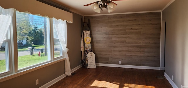 empty room with ceiling fan, dark hardwood / wood-style floors, wooden walls, and crown molding