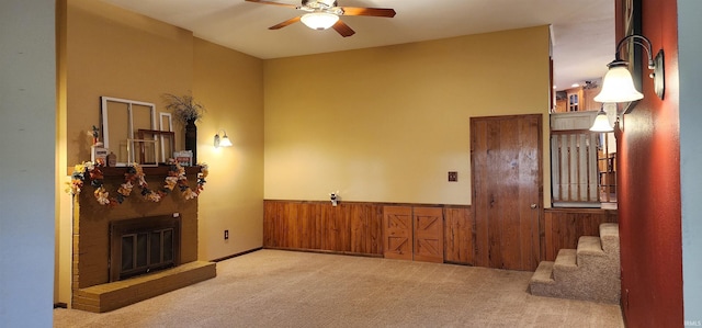 carpeted living room with wood walls, ceiling fan, and a brick fireplace