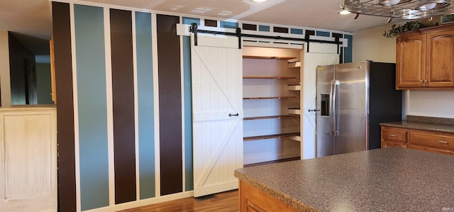 kitchen featuring a barn door, light wood-type flooring, stainless steel fridge with ice dispenser, and a textured ceiling