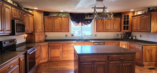 kitchen featuring wood-type flooring, a kitchen island, appliances with stainless steel finishes, a textured ceiling, and sink