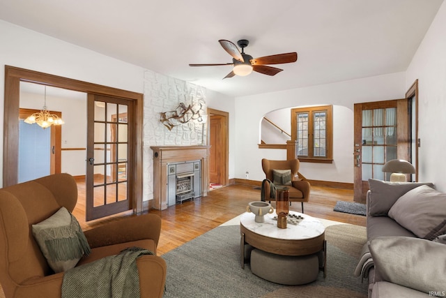 living room with a fireplace, ceiling fan with notable chandelier, light hardwood / wood-style flooring, and french doors