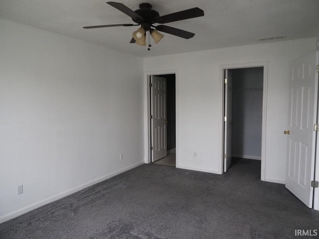 unfurnished bedroom featuring ceiling fan, dark colored carpet, a closet, and a spacious closet