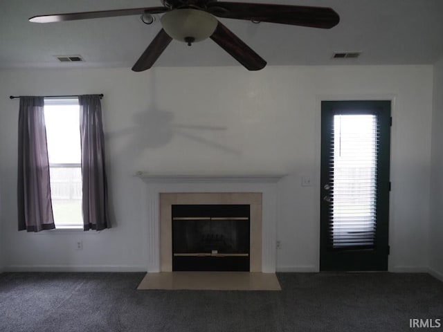 unfurnished living room featuring ceiling fan, a healthy amount of sunlight, and dark carpet