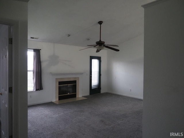 unfurnished living room featuring ceiling fan, a healthy amount of sunlight, and dark colored carpet