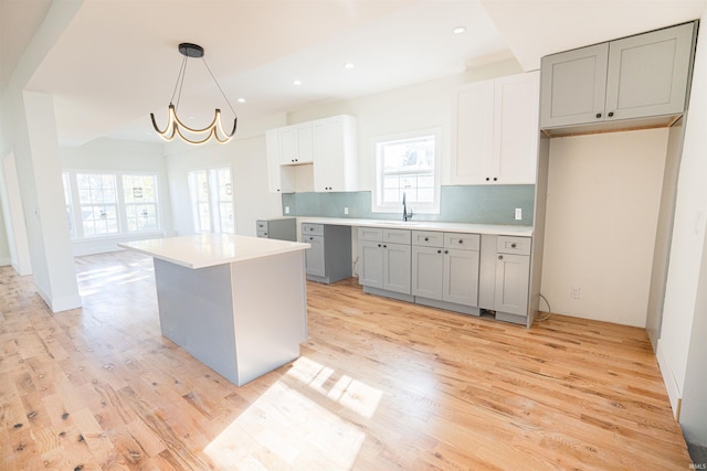 kitchen featuring white cabinetry, light hardwood / wood-style flooring, backsplash, pendant lighting, and a kitchen island