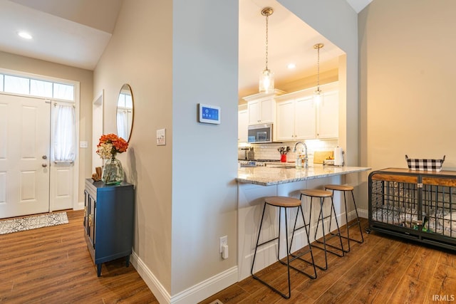 kitchen with a kitchen breakfast bar, white cabinetry, dark hardwood / wood-style floors, and pendant lighting