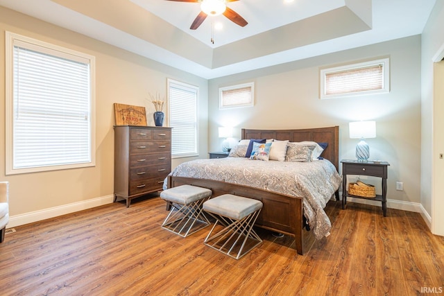 bedroom with hardwood / wood-style floors, ceiling fan, a tray ceiling, and multiple windows