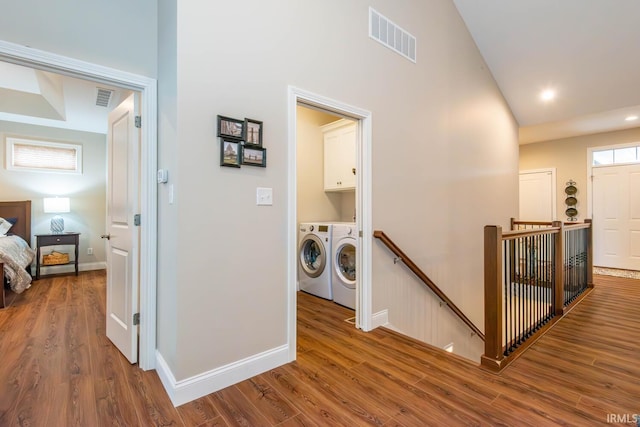 clothes washing area with separate washer and dryer, wood-type flooring, and cabinets