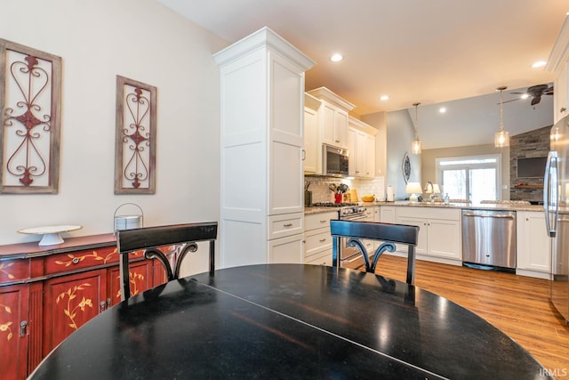 kitchen with backsplash, stainless steel appliances, vaulted ceiling, pendant lighting, and light hardwood / wood-style floors